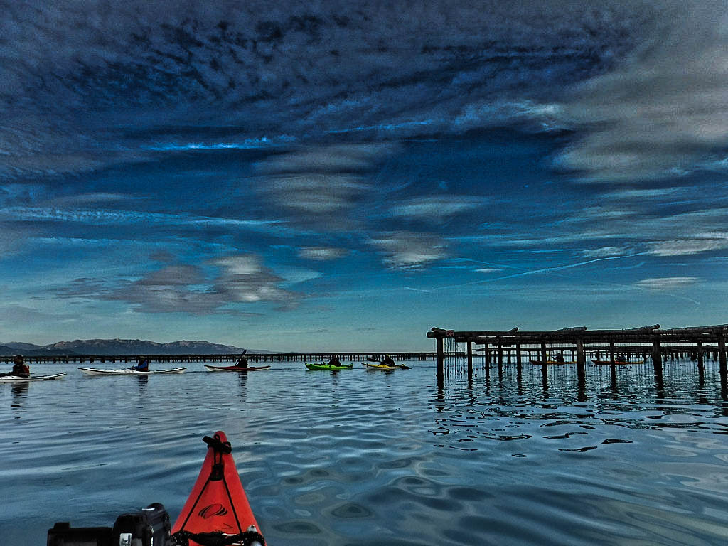 Kayakistas navegan entre las estructuras de cultivo marino, con un cielo dramático de fondo.
