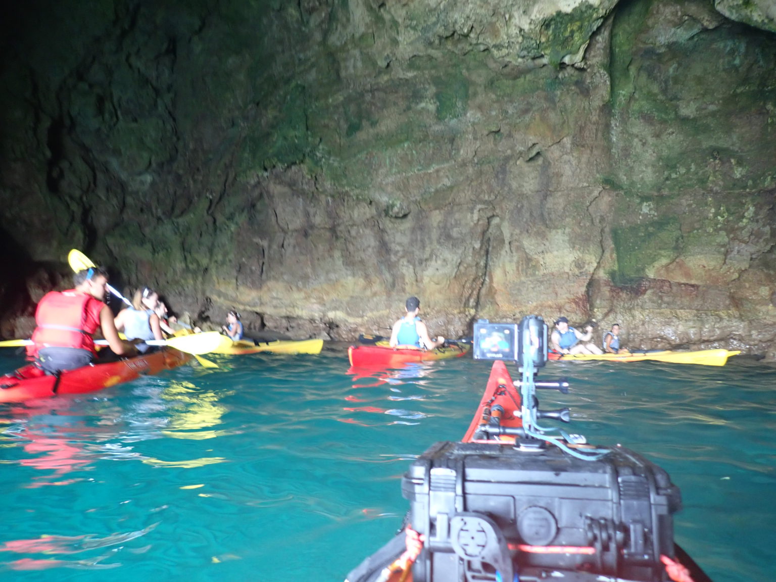 Un grupo de personas en kayaks explorando el interior de una cueva con formaciones rocosas y aguas turquesas.