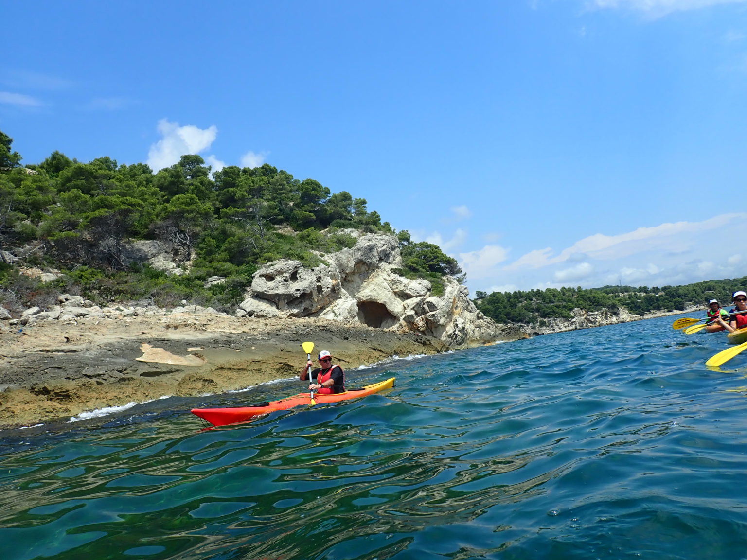 Un kayakista navegando en aguas claras cerca de una costa rocosa y arbolada.