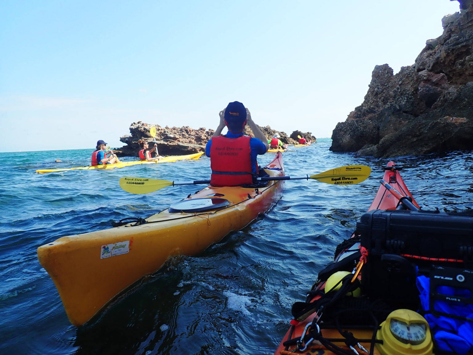 Vista desde un kayak de un grupo de personas remando en el mar abierto, rodeados de formaciones rocosas.