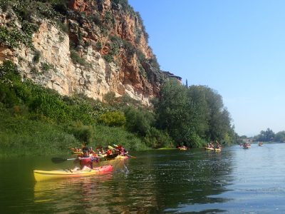 Kayakistas explorando las aguas del Ebro, con la imponente orografía de la ribera izquierda y la frondosa vegetación que define el paisaje fluvial.
