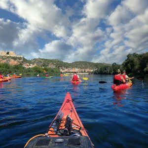 Un grupo de kayakistas disfruta de un tranquilo descenso por el río Ebro, con el majestuoso Castillo de Miravet al fondo.