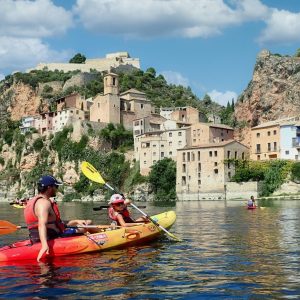 Disfrutando de un día de kayak en el río Ebro, pasando por el pintoresco Miravet bajo un cielo azul con nubes.