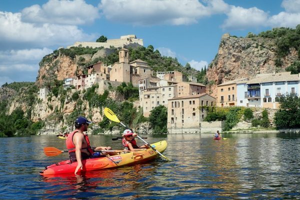 Disfrutando de un día de kayak en el río Ebro, pasando por el pintoresco Miravet bajo un cielo azul con nubes.
